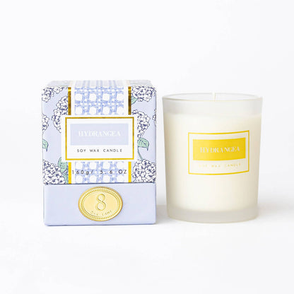 The Lillian Hydrangea Candle by 8 Oak Lane featuring a decorative floral design and a lit wick in a glass jar.