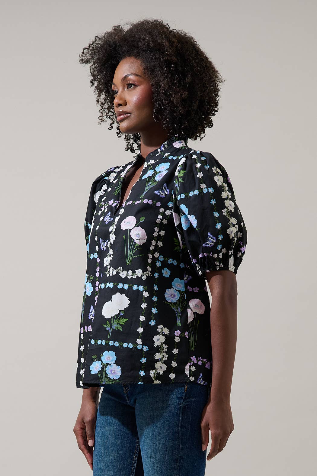 Sugarlips Trevis Noir Garden blouse, a stylish black top with floral details, displayed on a hanger with a blurred garden background.